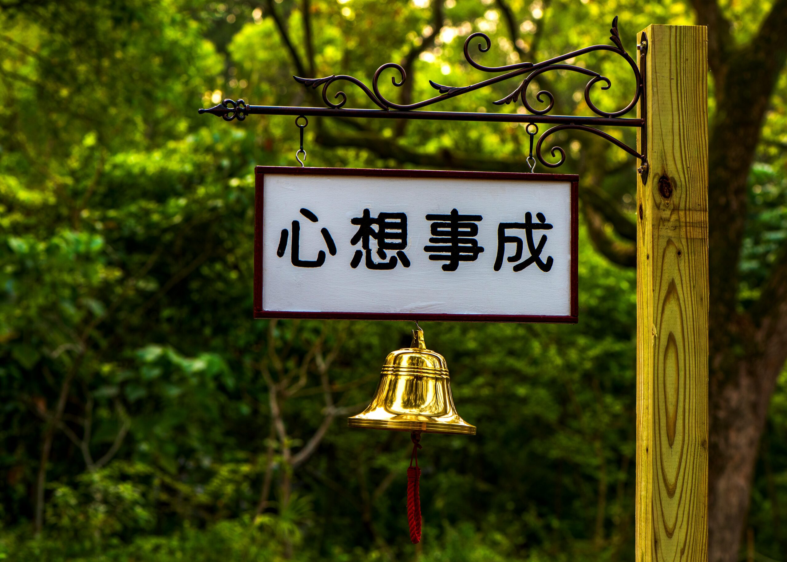 Outdoor signage with a golden bell in a lush Taipei park setting, conveying tranquility.